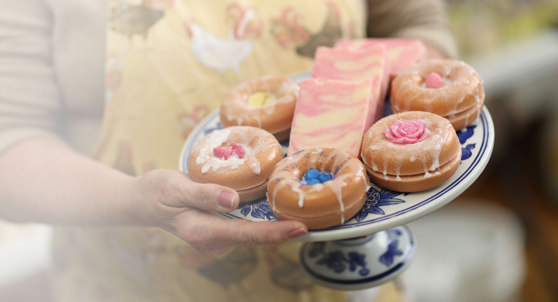 a cake plate with donut shaped soaps and a few bars of soap being held by the owner of morning mist soap
