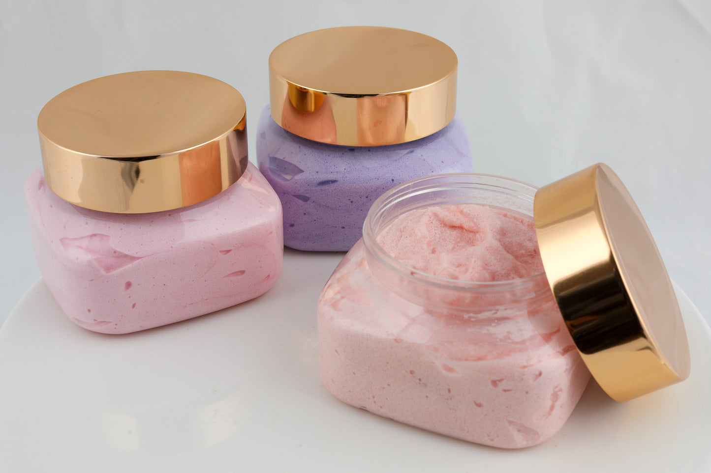 three jars of sugar soap in pink, peach, and purple with copper tops