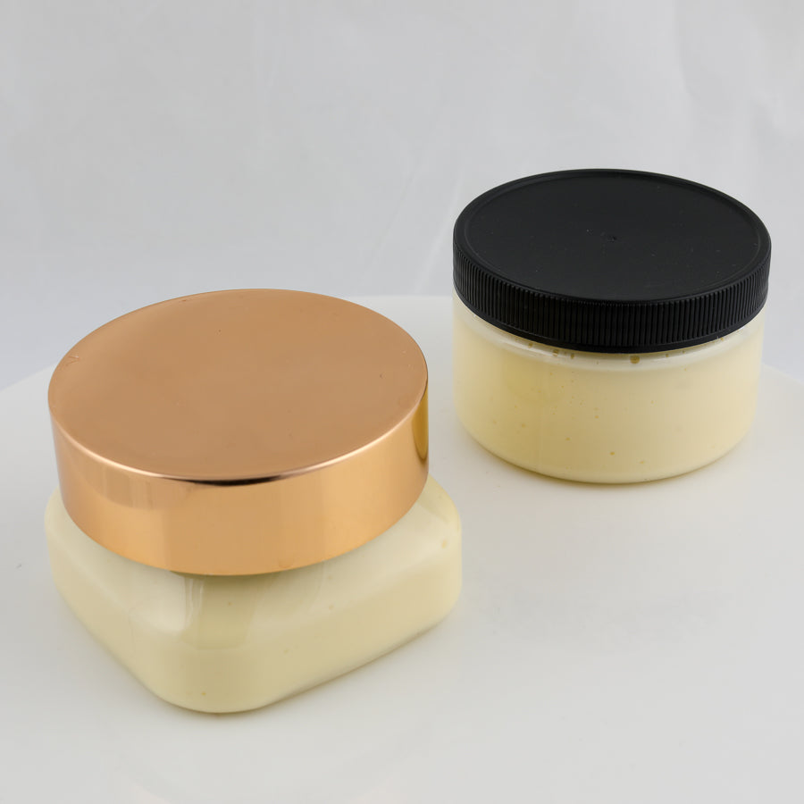 two jars of cream colored body butter. one with copper top and one with a black top.
