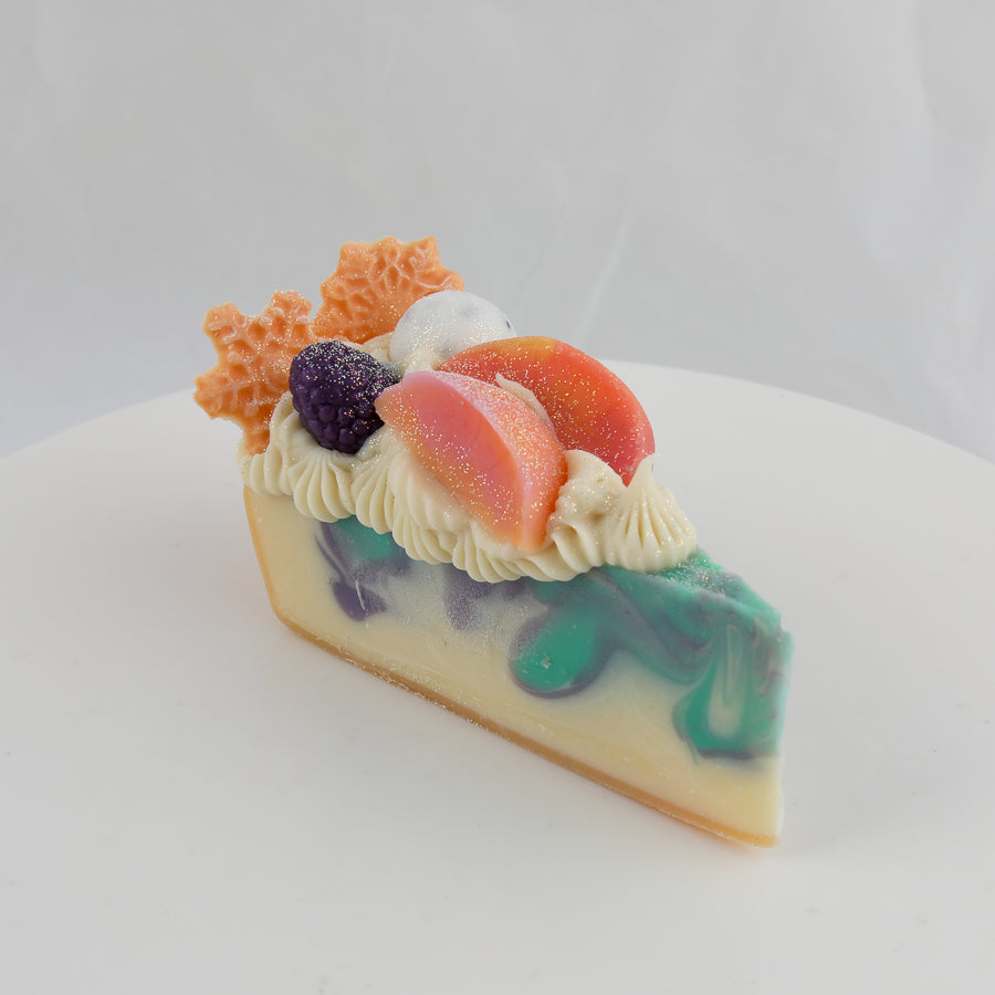 cream, green, and purple colored cake shaped soap with peach slices, blackberry, and snowflakes on top