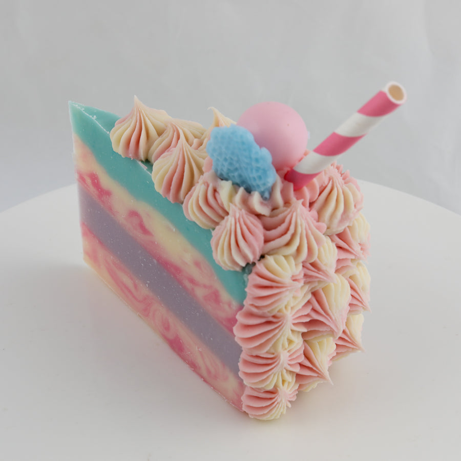 pink, purple, cream, and turquoise colored cake shaped soap with a straw and bonbon on top